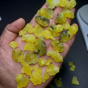 May include: A collection of yellow, translucent, irregularly shaped crystals with black inclusions. The crystals are scattered on a hand.