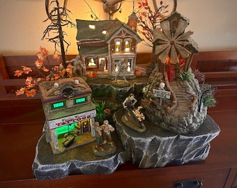 Könnte beinhalten: Eine Halloween-Dorfszene mit einem Spukhaus, einem Tattoo-Studio, einer Knochenmühle und einer Windmühle. Die Szene ist mit grünen und orangefarbenen Lichtern beleuchtet.