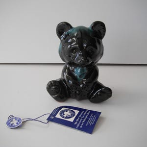 May include: Black ceramic bear figurine with blue and green glaze. The bear is sitting with its paws tucked in front of it. The figurine is part of a collection called "The Blue Mountain Collection - La Collection de la Montagne Bleue".