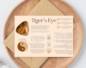 May include: A pink and white card with the words "Tiger's Eye" in a gold font. The card features a picture of a tiger's eye stone and information about the stone's healing properties, including its use in Feng Shui. The card also includes a diagram of the yin yang symbol.