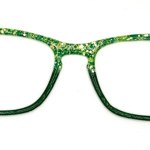 Op de afbeelding: Groene en witte glitterbril met een donkergroene gradi&euml;nt. De monturen hebben een rechthoekige vorm met afgeronde randen. De bril staat tegen een witte achtergrond.