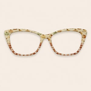 May include: Cat-eye glasses frames featuring a cream-colored background with a repeating pattern of small orange, green, and white pumpkins on the upper rims and a brown and white checkered pattern along the lower rims of the lenses.