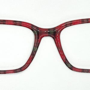 May include: Red and black plaid eyeglasses with a rectangular frame. The glasses have a bold, patterned design, with a classic tartan pattern. The frames are thick and sturdy, offering a stylish look. The lenses are clear, and the overall design is modern.