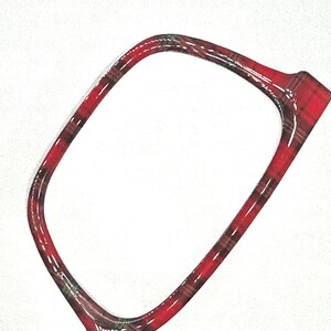 May include: A red and black plaid patterned frame, possibly for eyeglasses or a similar accessory, is set against a white background. The frame has a glossy finish and a rectangular shape with rounded corners.