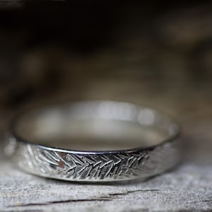 Puede incluir: Un anillo de plata con un diseño texturizado y estampado. El anillo está hecho de metal y tiene un acabado liso y pulido.