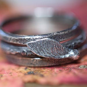Könnte beinhalten: Ein silberner Ring mit einem strukturierten Design und einem blattförmigen Detail. Der Ring besteht aus mehreren übereinander gestapelten Bändern.
