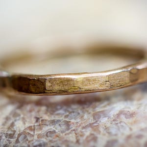 Op de afbeelding: Close-up van een gouden ring met een gehamerde textuur. De ring heeft een eenvoudig bandontwerp en een warme, metallic kleur. De ring is waarschijnlijk gemaakt van goud en is een sieraad.