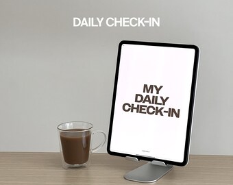 Puede incluir: Una tableta blanca con el texto "MY DAILY CHECK-IN" mostrado en la pantalla. La tableta está en un soporte plateado. Una taza de vidrio con líquido marrón está sobre una superficie de madera.