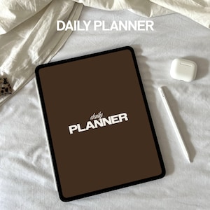 May include: A brown digital tablet with a black border and the text "daily PLANNER" in white on the screen. The tablet is lying on a white surface.