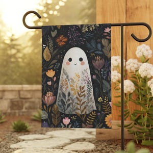 May include: A garden flag featuring a friendly ghost illustration. The ghost is white with a smiling face and is surrounded by colorful flowers and foliage against a dark background. The flag is displayed on a black metal stand.
