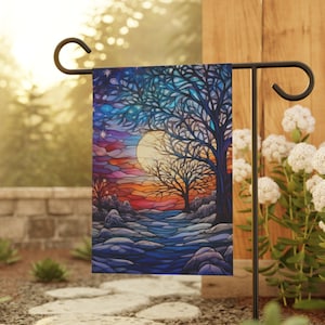 May include: A stained glass style garden flag with a blue, purple, and orange sunset scene. The flag features two trees with bare branches and a full moon in the sky.
