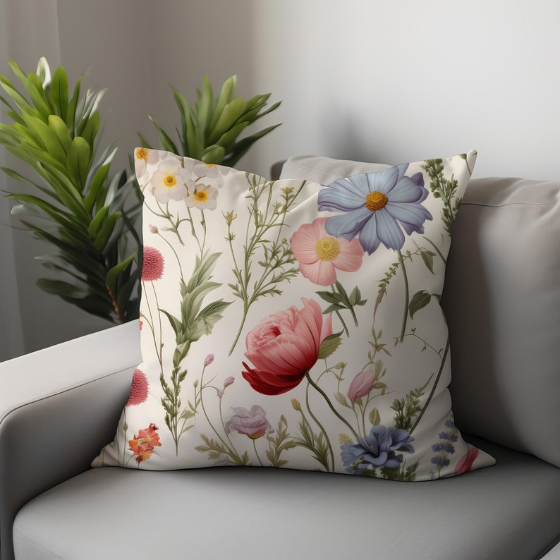 May include: A white cushion with a floral pattern featuring pink, blue, and red flowers. The cushion has a cream background and is decorated with a variety of flowers and leaves.