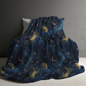 Può includere: Una coperta blu scuro caratterizzata da un motivo celeste con lune crescenti dorate, lune piene e stelle sparse su uno sfondo di nuvole blu navy e blu profondo. Il tessuto presenta un motivo ripetuto che raffigura il cielo notturno.