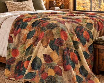 May include: A plush throw blanket featuring a vibrant pattern of autumn leaves in shades of red, orange, yellow, and dark green against a textured tan background, draped over a bed with layered pillows and a white duvet cover.