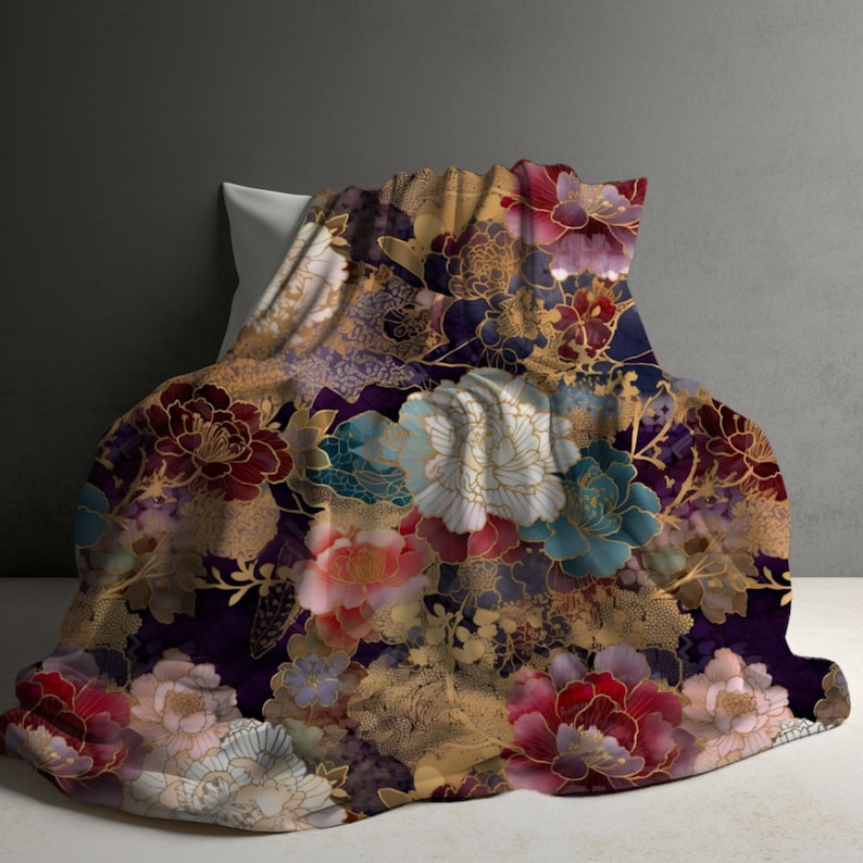 May include: A plush blanket with a floral design. The blanket features large, colorful flowers in shades of red, pink, blue, and white, set against a dark purple background. Gold accents highlight the floral pattern.