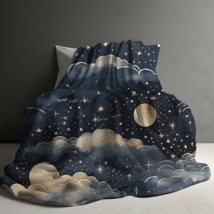Pode incluir: Uma manta azul-marinho escura com um padrão celestial de luas douradas, estrelas dispersas e nuvens suaves e ténues. O tecido apresenta um motivo de céu noturno com estrelas e luas de vários tamanhos por toda a superfície.