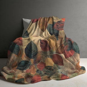 May include: A throw blanket featuring a autumnal leaf design in shades of brown, red, yellow, and green. The blanket is made from a soft, textured fabric and is ideal for adding a touch of autumn to your home.