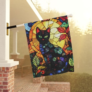 May include: A colorful stained glass style garden flag featuring a black cat with green eyes. The cat is sitting in the center of the flag, surrounded by a variety of colorful leaves and flowers.