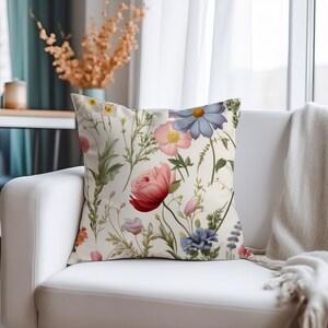 May include: A white cushion with a floral pattern featuring pink, red, blue, and yellow flowers. The cushion has a cream background and is decorated with a variety of floral designs.