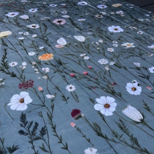 May include: A blue fabric with a white floral pattern. The fabric features a variety of white flowers, including daisies, cosmos, and other wildflowers. The fabric is perfect for crafting projects, such as quilts, pillows, and tablecloths.