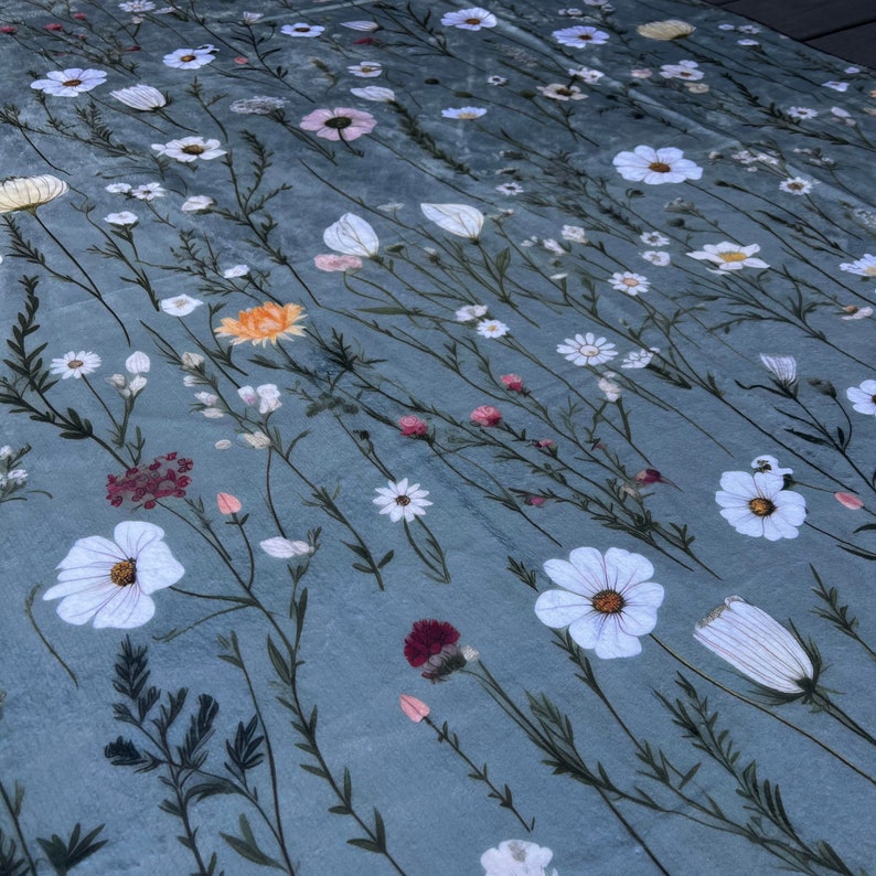 May include: A blue fabric with a white floral pattern. The fabric features a variety of white flowers, including daisies, cosmos, and other wildflowers. The fabric is perfect for crafting projects, such as quilts, pillows, and tablecloths.
