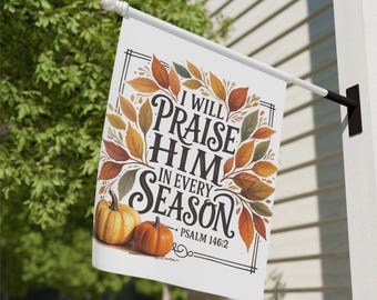 Puede incluir: Una bandera blanca para exteriores con el texto "I WILL PRAISE HIM IN EVERY SEASON" y Salmo 146:2. La bandera presenta un borde de hojas de otoño y dos calabazas. La bandera está montada en un mástil blanco.