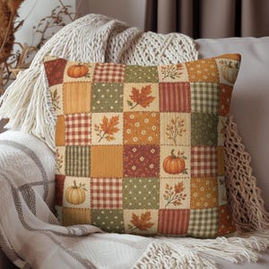 May include: A square throw pillow featuring a patchwork design with alternating squares of autumn-themed patterns. The print includes orange pumpkins, brown maple leaves, green polka dots, red and white gingham, and small floral motifs.