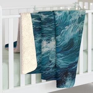 May include: A plush throw blanket featuring a printed design of deep blue ocean waves with white sea foam. The reverse side of the blanket is made of a cream-colored, textured sherpa fleece material, providing a soft and fuzzy surface texture.