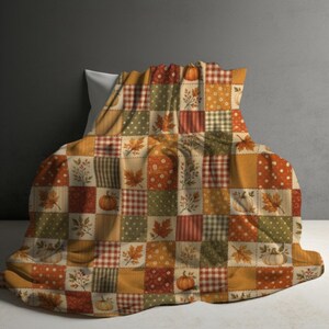 Op de afbeelding: Een patchwork deken met een herhalend raster van vierkanten in herfstkleuren zoals oranje, olijfgroen en crème. Het patroon toont diverse motieven zoals pompoenen, esdoornbladeren, stippen en ruitjes in een seizoensgebonden ontwerp.