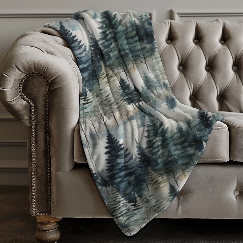 May include: A soft, plush throw blanket with a watercolour print of a forest scene. The blanket features a repeating pattern of pine trees in shades of green, blue, and grey, with a subtle snowfall effect.
