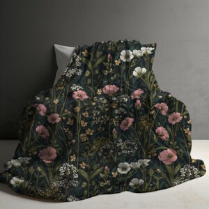 May include: A dark green floral blanket with pink, white, and yellow flowers. The blanket is draped over a white pillow, creating a cozy and inviting scene. The floral pattern is detailed and intricate, with various types of flowers and foliage.