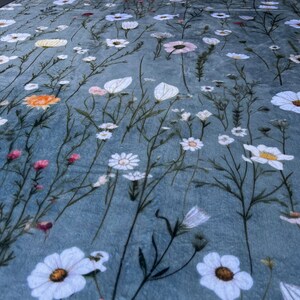 May include: A blue fabric with a white floral pattern. The fabric features a variety of white flowers, including daisies and other delicate blooms.