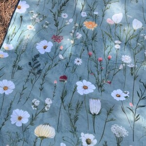 May include: A blue fabric picnic blanket with a floral pattern featuring white flowers and green leaves.