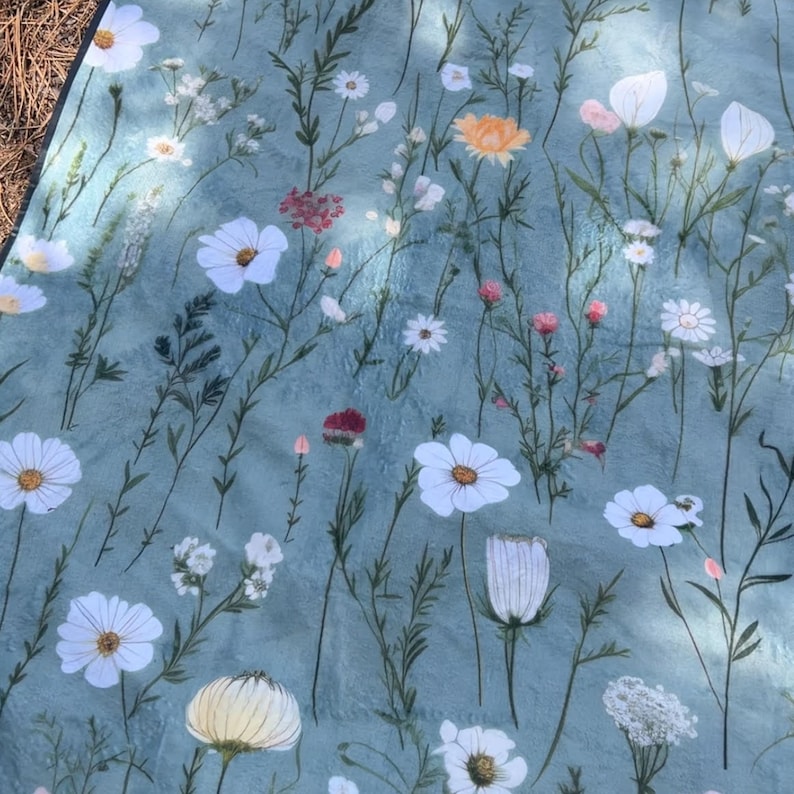 May include: A blue fabric picnic blanket with a floral pattern featuring white flowers and green leaves.