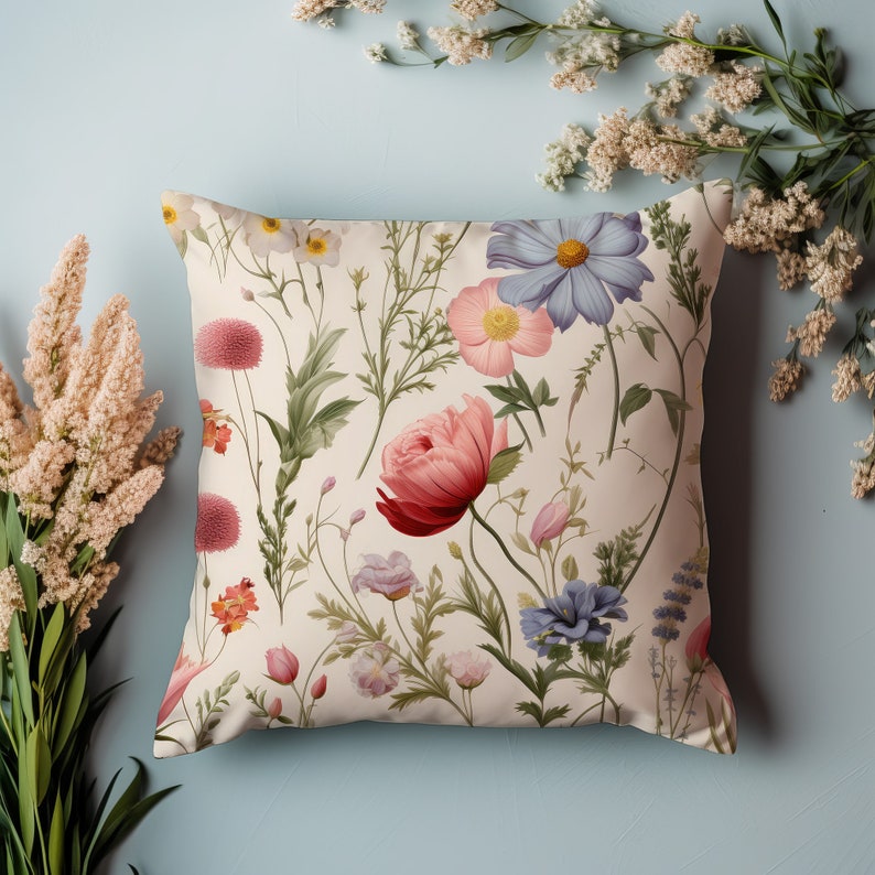 May include: A cream-coloured throw pillow with a floral pattern featuring pink, red, blue, and white flowers. The pillow has a subtle cream background and a variety of floral designs.
