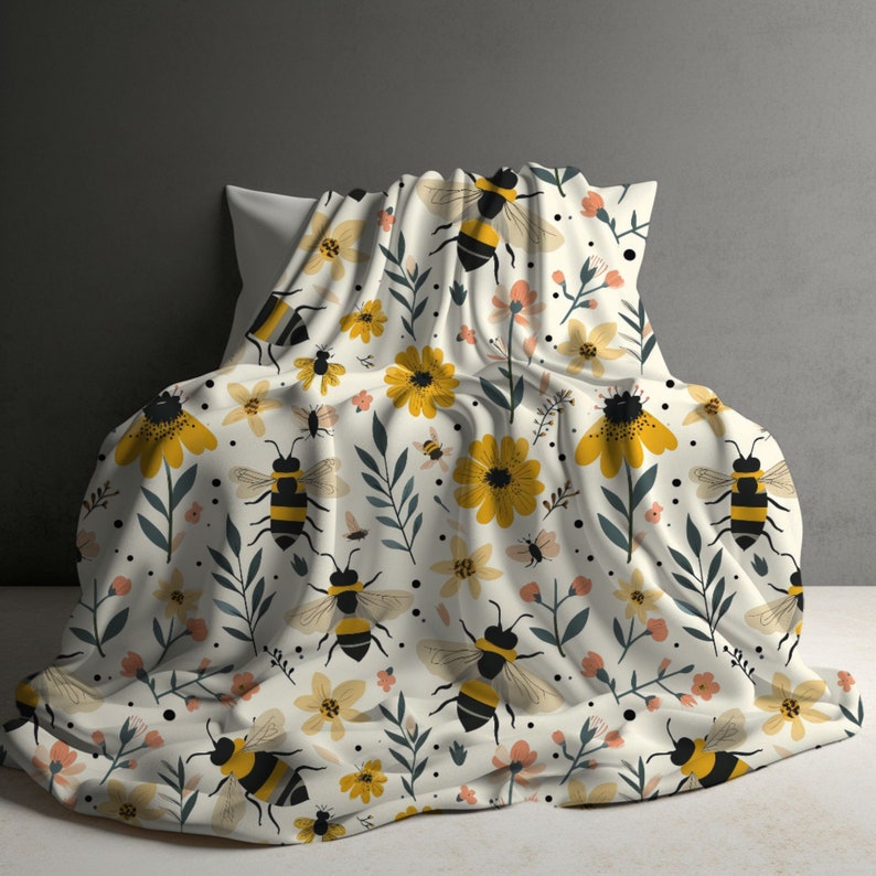 May include: A white throw blanket with a repeating pattern of yellow flowers, green leaves, and black and yellow bees.