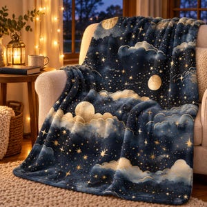 May include: A plush throw blanket featuring a dark navy blue background with a celestial pattern of golden yellow stars, crescent moons, and soft, fluffy clouds. The fabric has a smooth, velvety texture and drapes over a light-colored armchair.