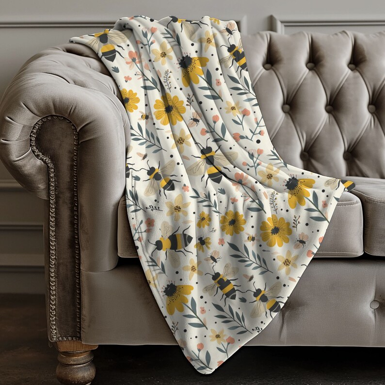 May include: A white fleece throw blanket with a pattern of yellow flowers, green leaves, and black and yellow bees.