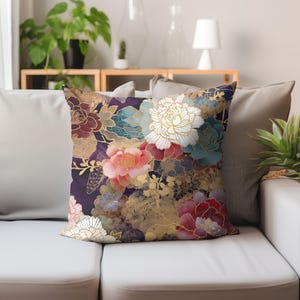 Puede incluir: Una almohada decorativa con un patr&oacute;n floral que presenta flores rosas, blancas y azules sobre un fondo morado oscuro con detalles dorados.
