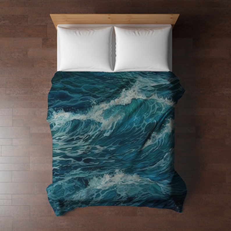 May include: A bed comforter featuring a detailed illustration of deep blue ocean waves with white sea foam crests. The bedding is paired with two plain white pillows, creating a contrast between the dark, textured water pattern and the solid white.