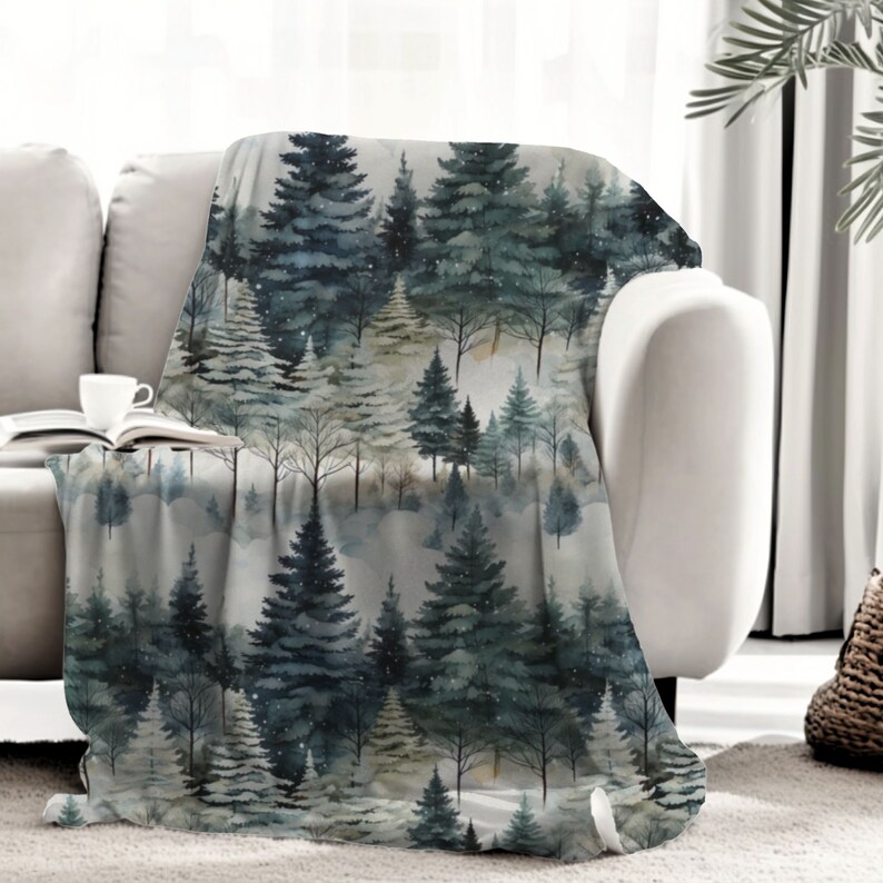 May include: A soft, plush throw blanket featuring a watercolour-style pattern of a snowy forest with pine trees. The background is a light grey with a subtle shimmer.