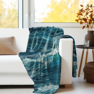 May include: A rectangular throw blanket featuring a detailed graphic print of deep blue ocean waves with white sea foam crests. The fabric displays a continuous pattern of turbulent water, showing various shades of navy, teal, and bright white.