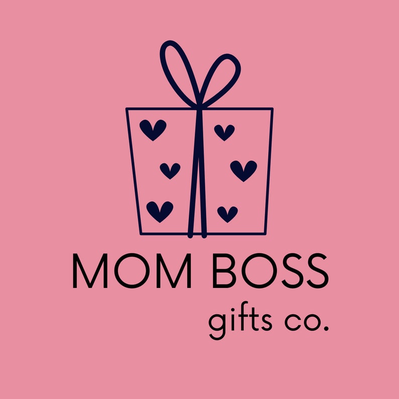May include: A pink background with a navy blue gift box illustration adorned with hearts and a bow. The text "MOM BOSS gifts co." is displayed in black, indicating a gift-related business.