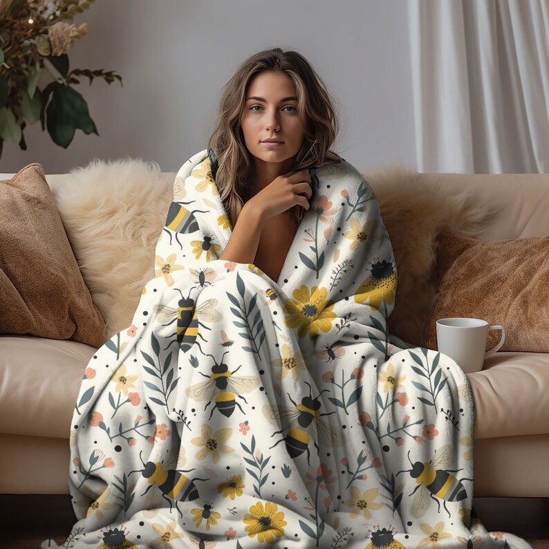 May include: A white fleece throw blanket with a repeating pattern of bees, flowers, and leaves. The blanket is soft and cozy, perfect for snuggling up on the couch.