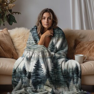 May include: A soft, white fleece blanket with a watercolour print of a snowy forest. The blanket features a repeating pattern of dark green pine trees and a light blue sky with white snowflakes.