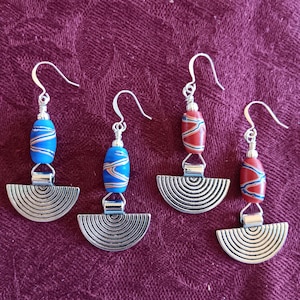 May include: Four pairs of dangle earrings. Each earring features a silver-tone, half-circle pendant with concentric lines. The earrings have a beaded accent in blue and red, or red and white, and a silver-tone hook.