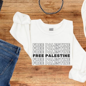 Könnte beinhalten: Weißes Sweatshirt mit dem Spruch "FREE PALESTINE", der fünfmal in schwarzer Schrift wiederholt wird.