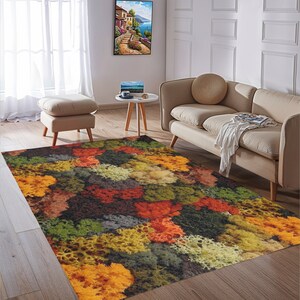 May include: A colorful area rug with a vibrant, abstract pattern. The rug features a mix of orange, yellow, green, and brown hues, creating a textured, natural look. It's placed in a living room setting with neutral-toned furniture and decor.