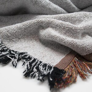 May include: A gray and white woven throw blanket with a brown and black fringe. The blanket has a textured woven pattern.