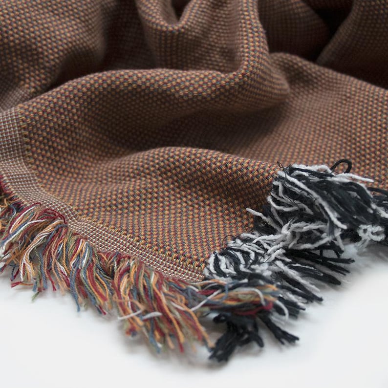 May include: A brown and orange woven throw blanket with a fringe border. The fringe is a mix of black, white, red, and blue.